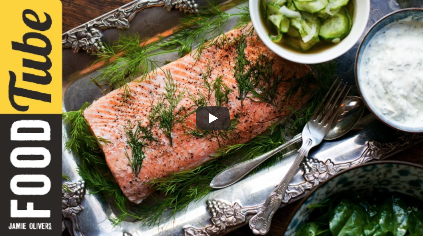 Image of poached salmon on a plate with dill and white sauce with silverware beside the fish