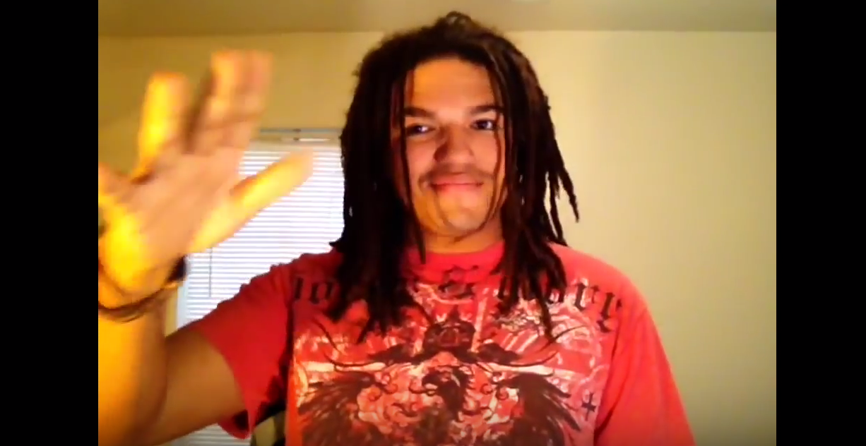 A person with shoulder-length dread locks wearing a red shirt with white background