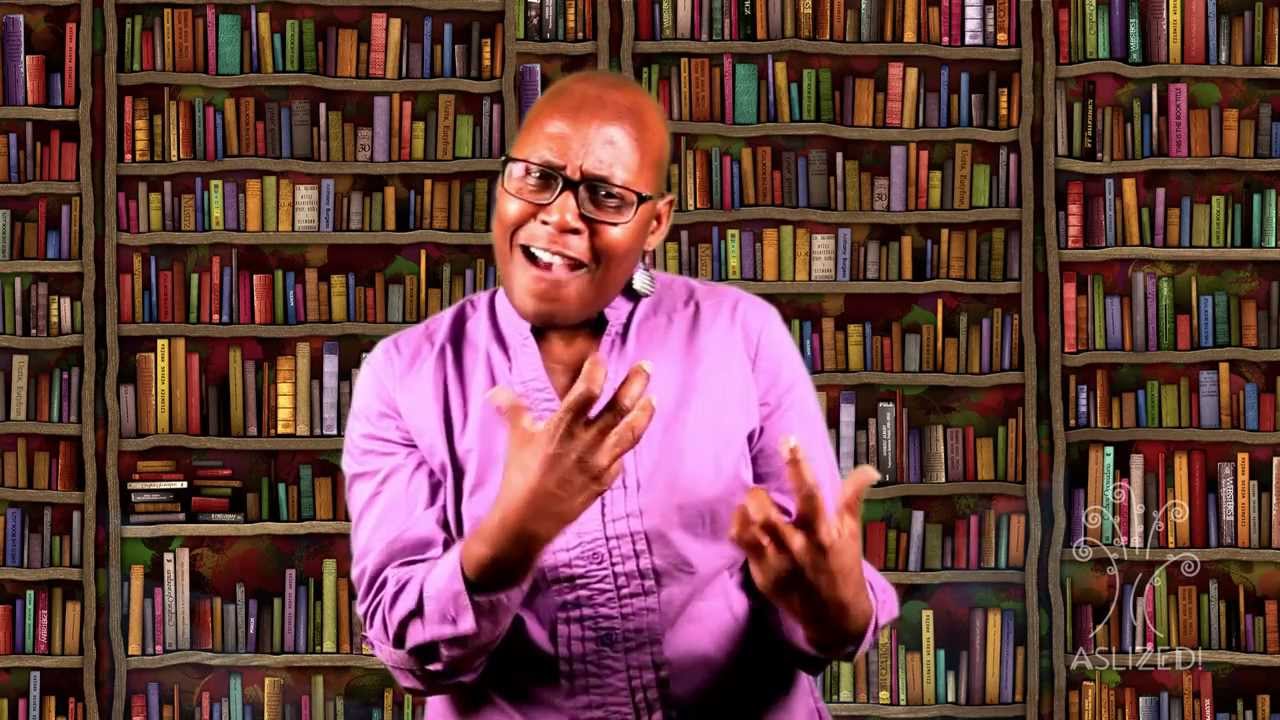 An African-American woman wearing a purple shirt stands in front of a bookshelf