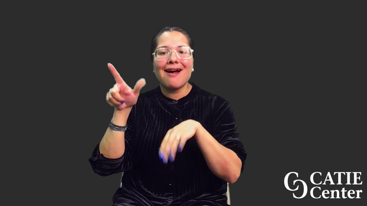 A woman with fair skin is wearing a black blouse with light vertical stripes down the front.  She is wearing wire-rimmed glasses and has her dark hair pulled back.  She sits in front of a dark grey background and narrates the entire story.  In the lower right corner of the video screen is a white CATIE Center logo