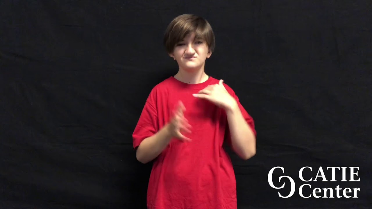 A white non-binary person wears red baggy short-sleeve shirt and is shown from the waist up. The person is standing in front of a dark-grey screen. A white CATIE Center logo is in the lower right corner of the screen. The person narrates the entire video in American Sign Language.