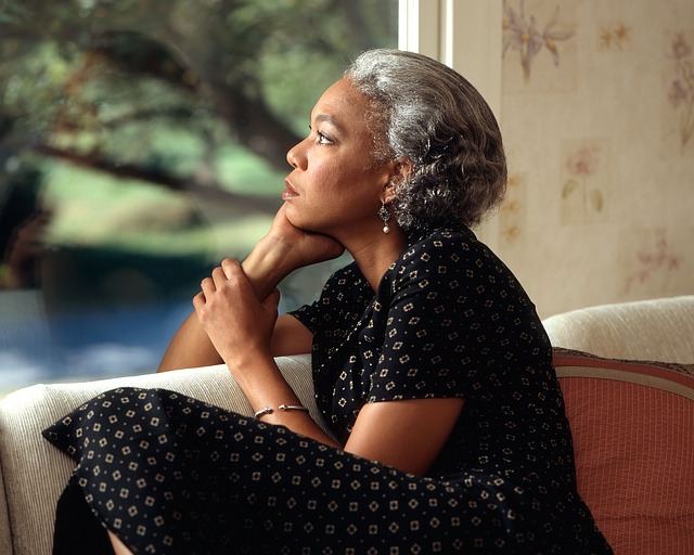 Woman with grey hair sits by window pensively looking outside