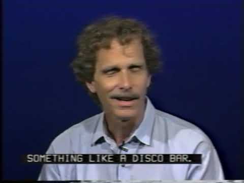 A white man with curly brown hair and a mustache wearing a blue collared shirt sits in front of a dark blue background. An open cation reads Something like a Disco Bar