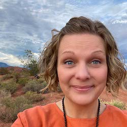 A white woman with short blond hair wearing orange shirt in the Utah desert